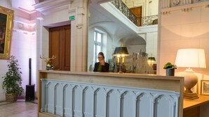 A reception area with a wooden reception desk, a large mirror, and a staircase in the background.