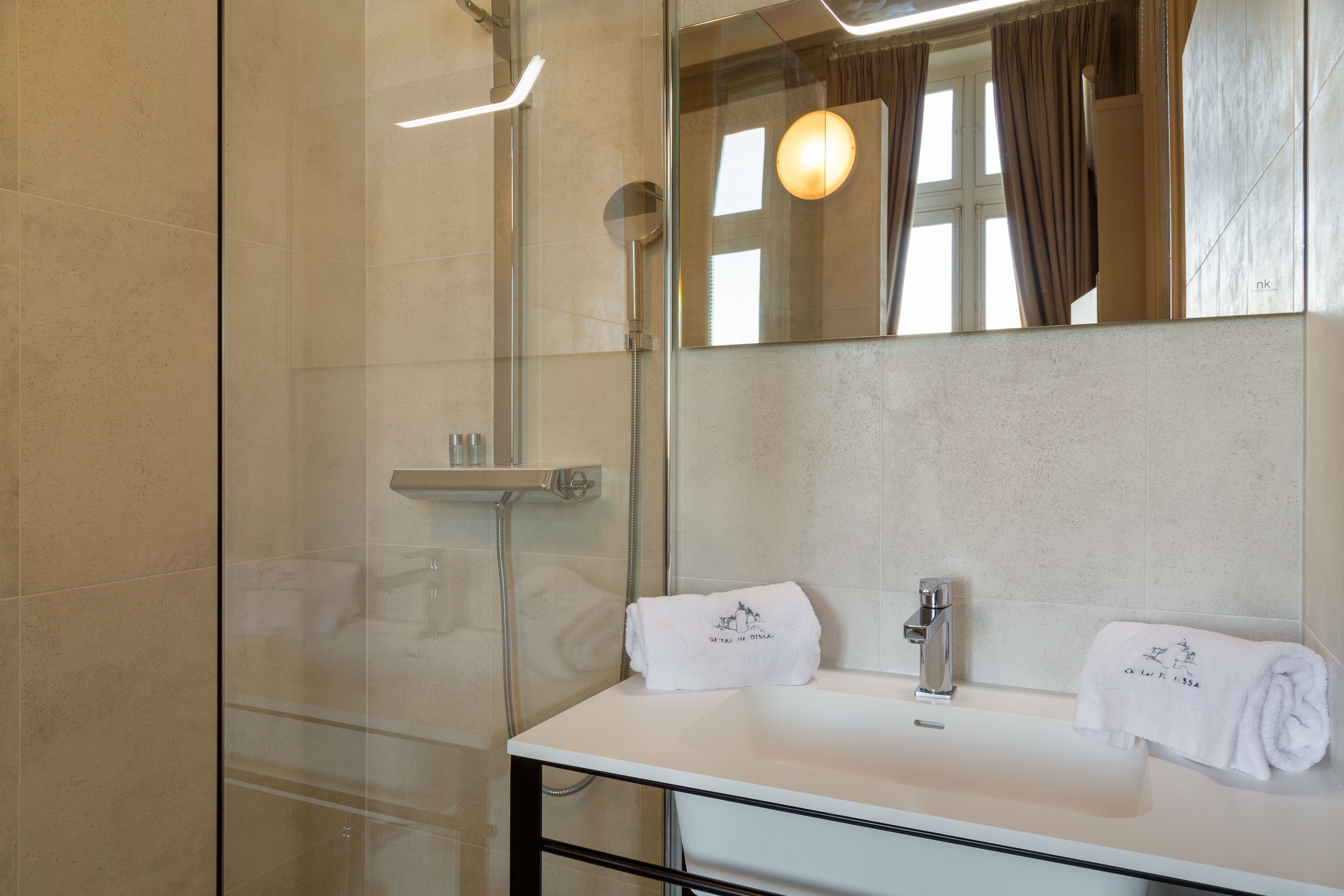 Un bagno moderno con box doccia in vetro, un lavandino bianco con specchio sopra e due asciugamani con un logo.