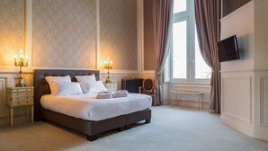 A spacious bedroom with a large bed, two bedside tables with lamps, a small table, and a TV mounted on the wall.