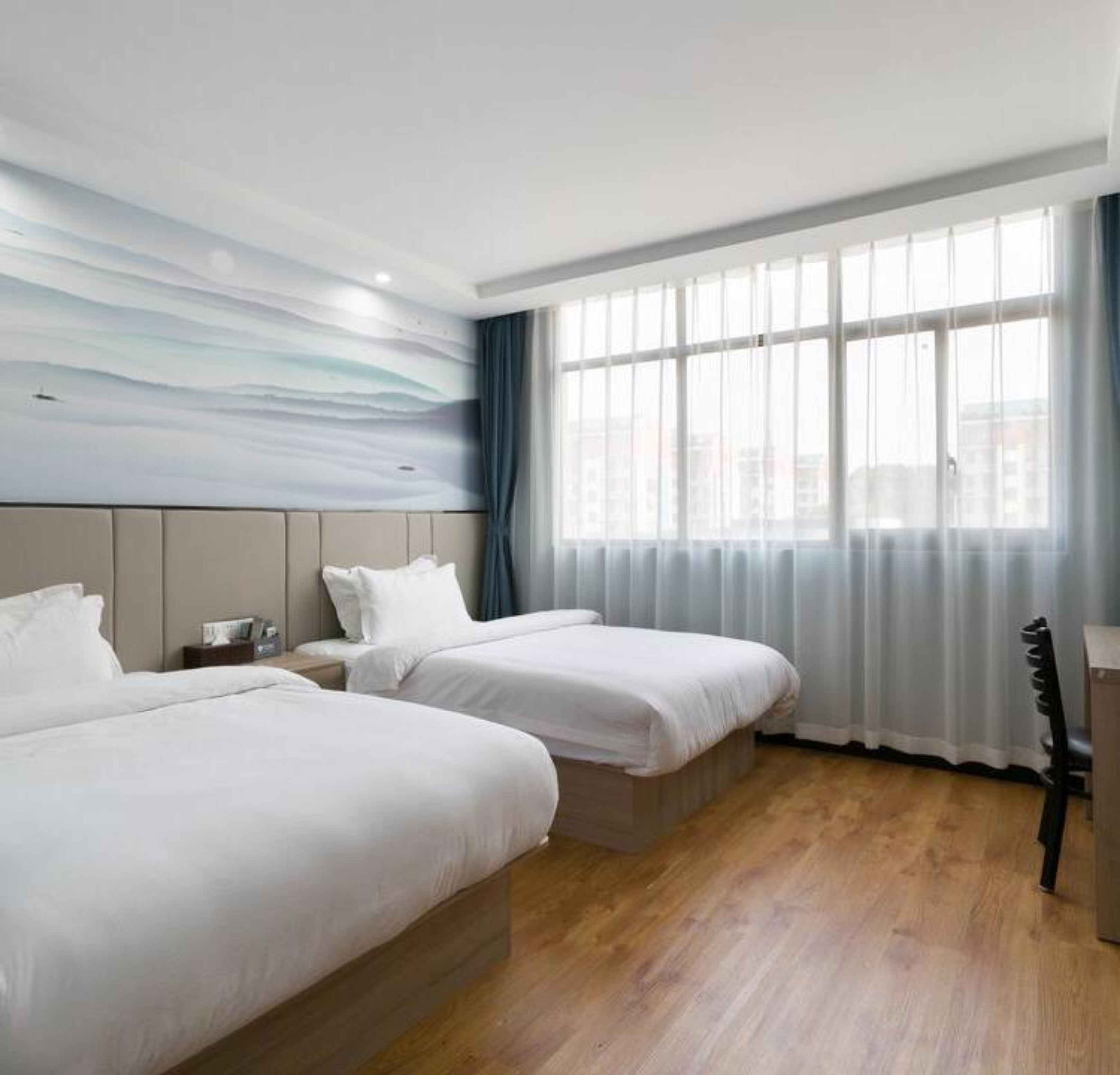 A hotel room with two beds, a large window with curtains, a headboard with a wave-patterned wall, and a wooden floor.