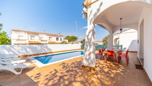 Zona de piscina con tumbonas y mesa lista para comer, rodeada de paredes blancas y cielo despejado.