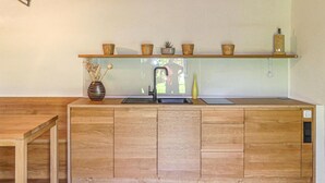 A wooden kitchen with a built-in sink, a shelf above the sink holding baskets and a plant, and a vase with dried flowers on the left. - Ferienhaus Deutsch Schuetzen (Deutsch Schützen)