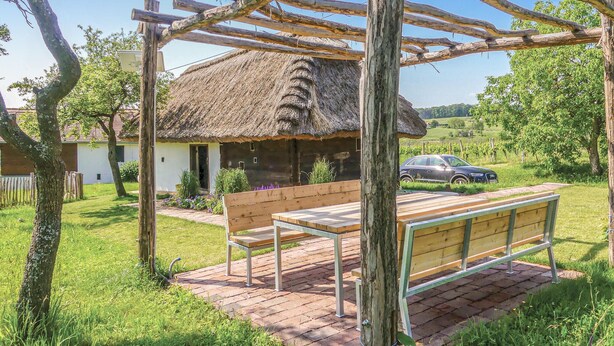 A rustic outdoor seating area with a bench and table, a thatched-roof structure, and a car parked nearby. - Ferienhaus Deutsch Schuetzen (Deutsch Schützen)