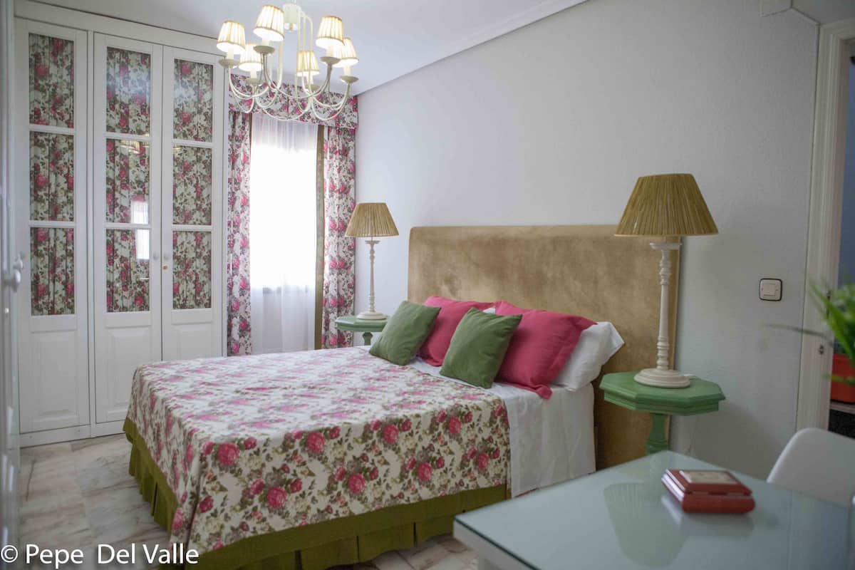 Quarto com cama, duas luminárias de cabeceira, mesa de cabeceira, cadeira e mesa com um livro.