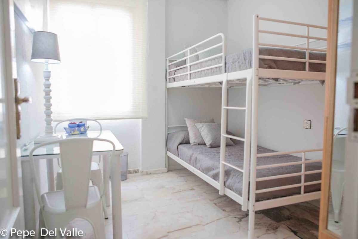 Quarto com beliche, mesa, cadeiras, luminária e janela.