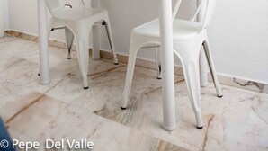 Un coin repas avec une table en verre, des chaises blanches, une lampe blanche et un tableau représentant un voilier accroché au mur.