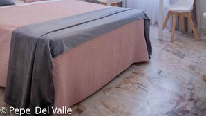 Une chambre d’hôtel avec un grand lit, une table de chevet, une petite table avec des chaises, une fenêtre avec des rideaux et un luminaire au plafond.