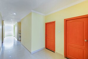 A hallway with two orange doors, a water dispenser, and a white ceiling with recessed lighting. - OYO 30151 Golden Hive (Hyderabad)
