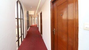 A corridor with a red carpet, wooden doors, and large windows on one side. - OYO 30593 Heritage Corner (Patiala)