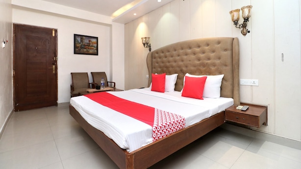 A neatly arranged hotel room with a large bed, a wooden nightstand, a desk, and a chair. - OYO 30593 Heritage Corner (Patiala)