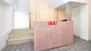 A staircase with a wooden handrail and a pink reception desk with a sign indicating operating hours. - OYO 30593 Heritage Corner (Patiala)