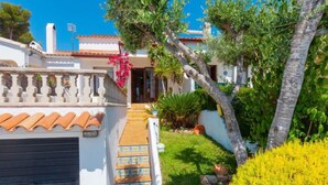 A white building with a tiled roof, a garage door, and a staircase leading to a door. - Remedios by Interhome (Cunit)