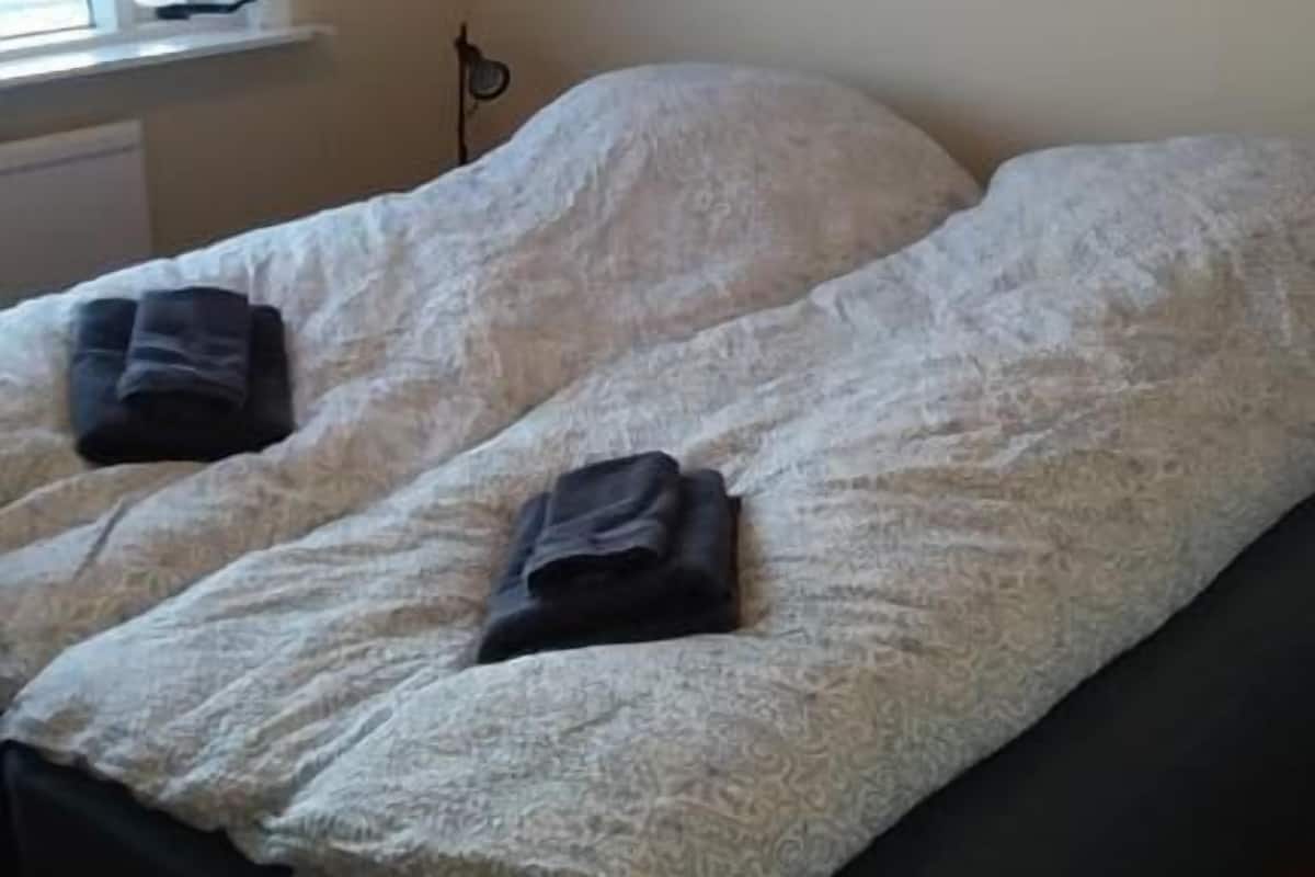 A room with two beds, a window with curtains, a framed picture on the wall, and a radiator.
