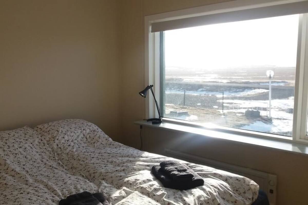A bedroom with a bed covered in floral bedding, a bedside lamp, and a view of a snowy landscape through a window.