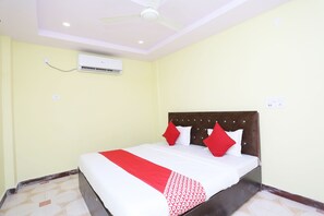 Una habitación de hotel con cama, ventilador de techo, unidad de aire acondicionado y piso de baldosas.