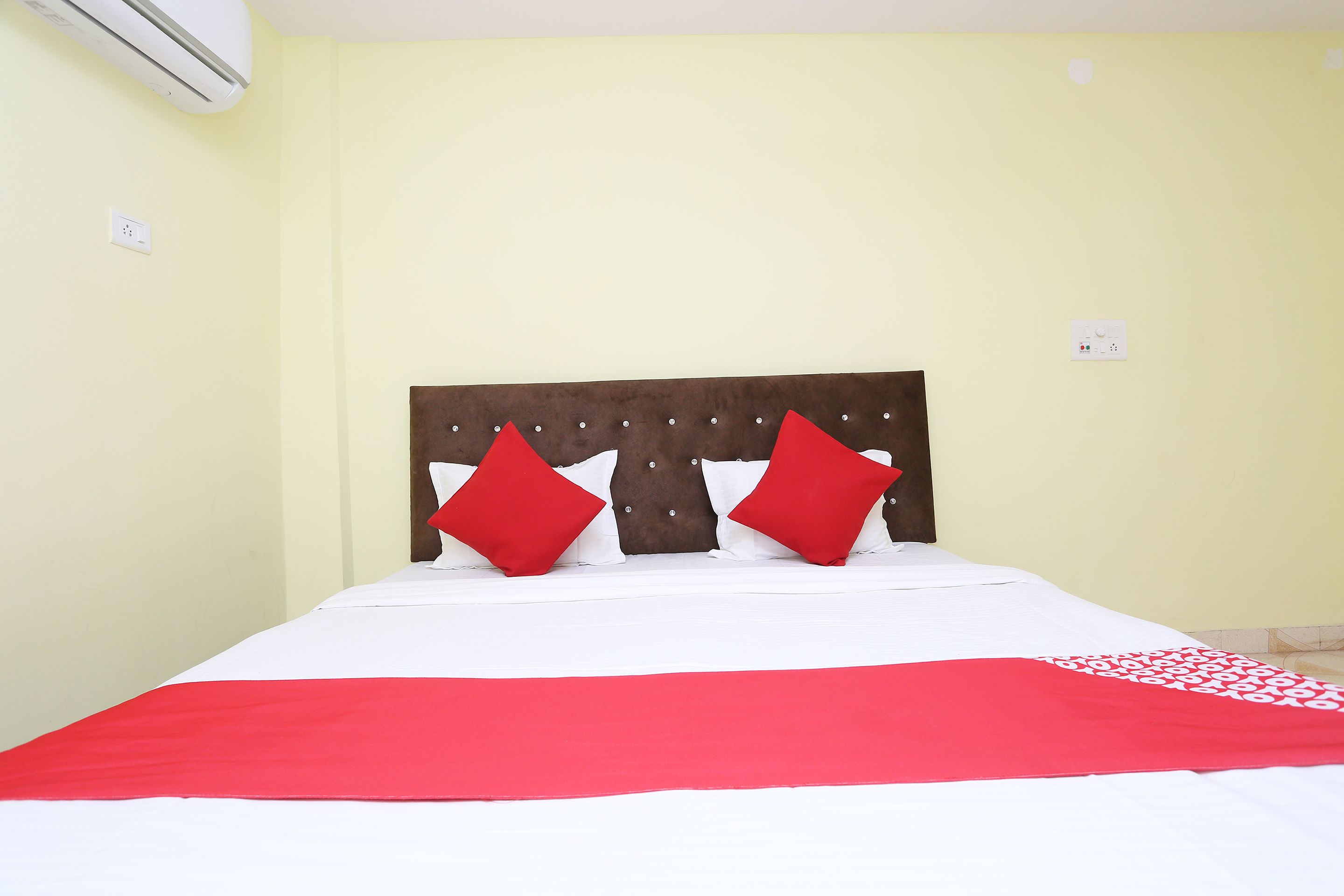 Una cama con una colcha blanca y roja, dos almohadas rojas y un cabecero marrón.