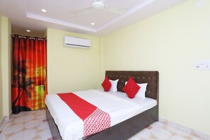 Una habitación de hotel con cama, ventilador de techo, equipo de aire acondicionado y cortina de ducha con diseño tropical.