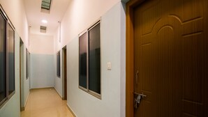 Een gang met een houten deur, een raam en een lichtschakelaar op de muur.