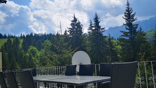 An outdoor patio with a table and chairs, overlooking a forested area and mountains. - BonDia (Rasnov)