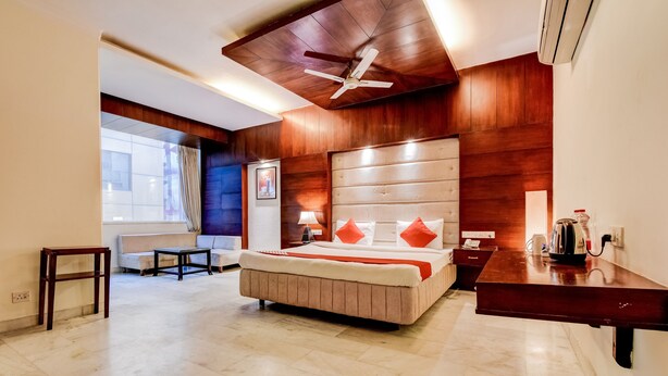 A hotel room with a large bed, a desk, a chair, a ceiling fan, and a window with curtains. - OYO 39725 Hotel Regent Continental (New Delhi)