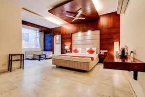 Habitación de hotel con una cama grande, un escritorio, una silla, un ventilador de techo y una ventana con cortinas.