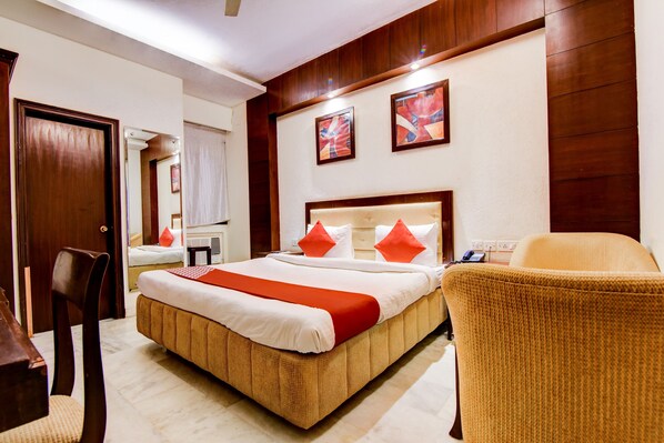 A hotel room with a large bed, a chair, a desk, and a mirror.