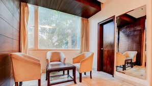 A room with a wooden floor, a large window with curtains, two armchairs, a small table, and a mirror reflecting the room. - OYO 39725 Hotel Regent Continental (New Delhi)