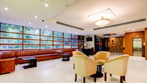 A spacious lobby with a leather sofa, armchairs, a travel desk, and large windows with a view. - OYO 39725 Hotel Regent Continental (New Delhi)