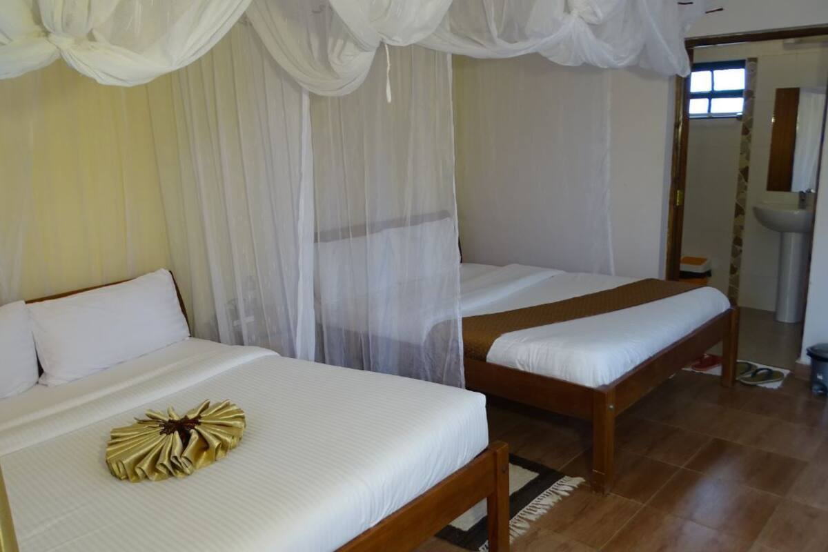 A room with two beds, each with white bedding and a canopy. There is a small table with a gold decorative item on one bed.