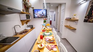 Una cocina estrecha con una mesa de desayuno dispuesta y un televisor montado en la pared, junto con diversos electrodomésticos.