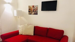 Un sofá seccional rojo con un cojín blanco, un televisor de pantalla plana negro y un cuadro en la pared.