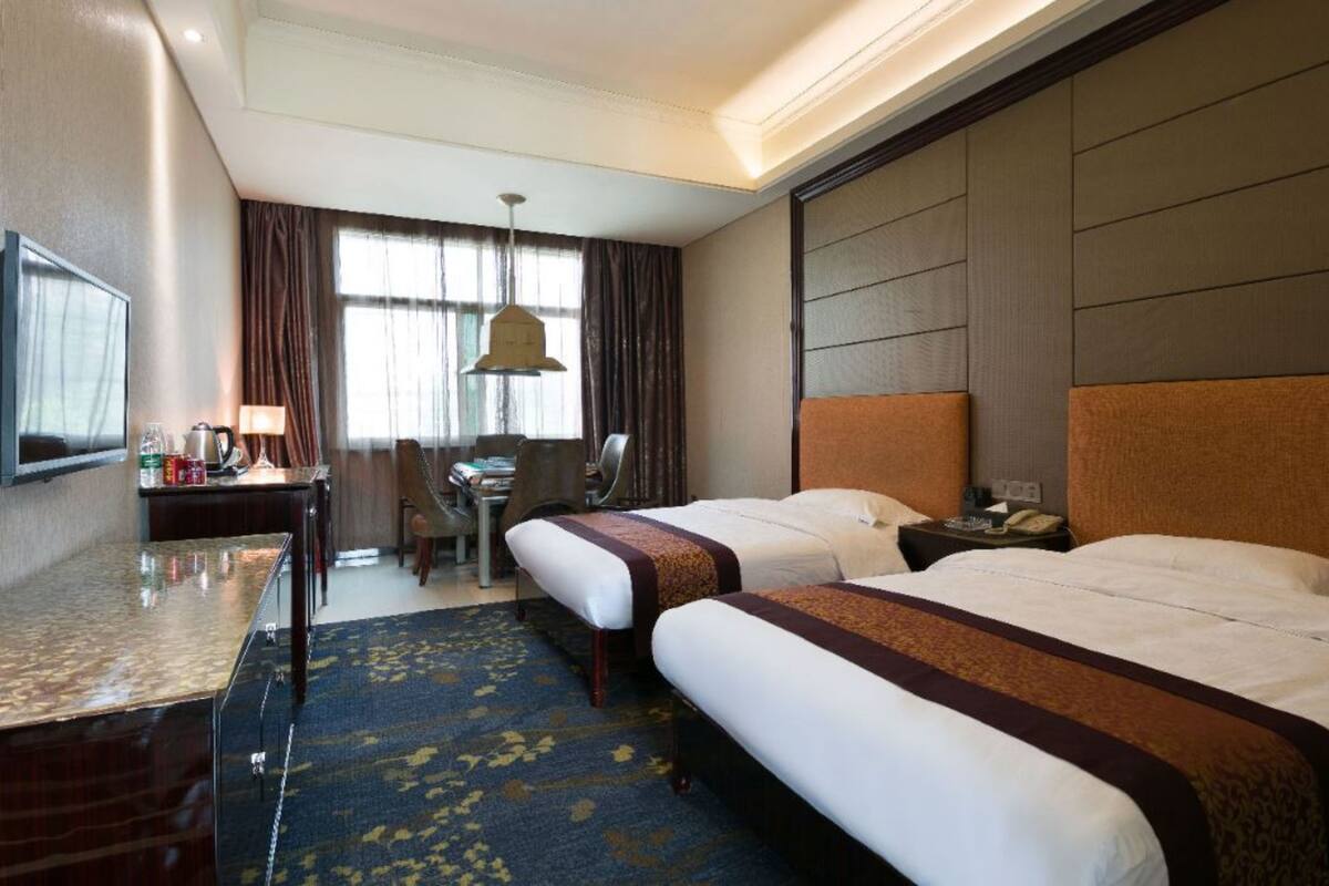 A hotel room with two beds, a desk, a chair, a TV, and a window with curtains.