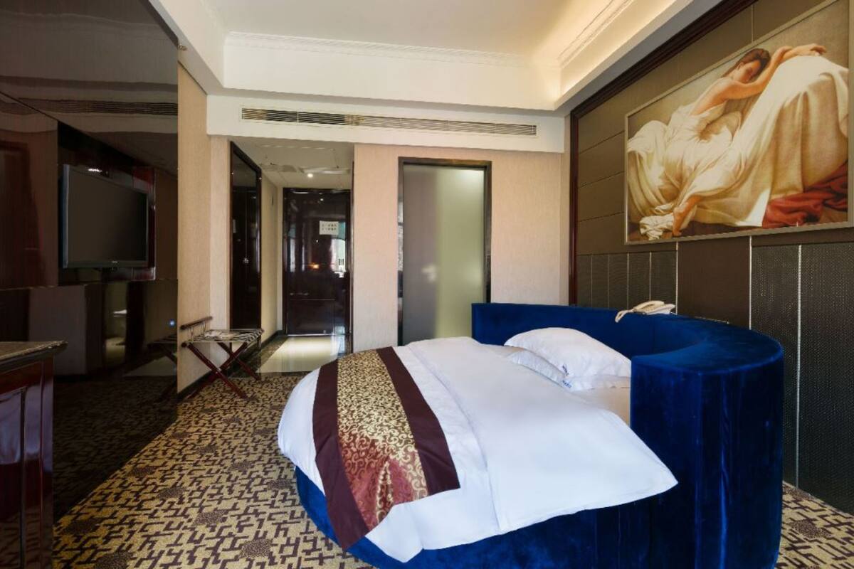 A hotel room with a bed, a television, a desk, and a painting on the wall.