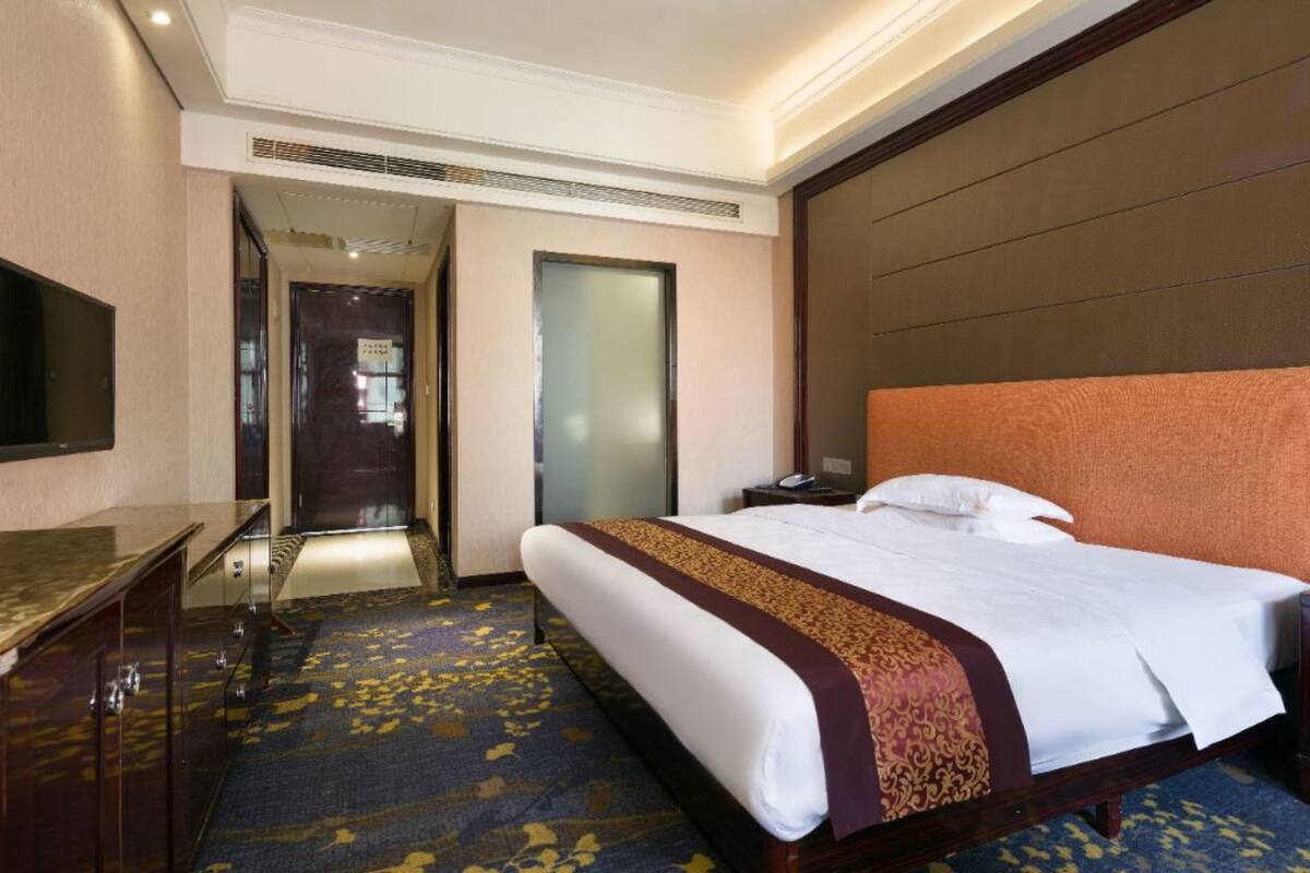 A hotel room with a large bed, a desk, a flat-screen TV, and a door leading to a hallway.