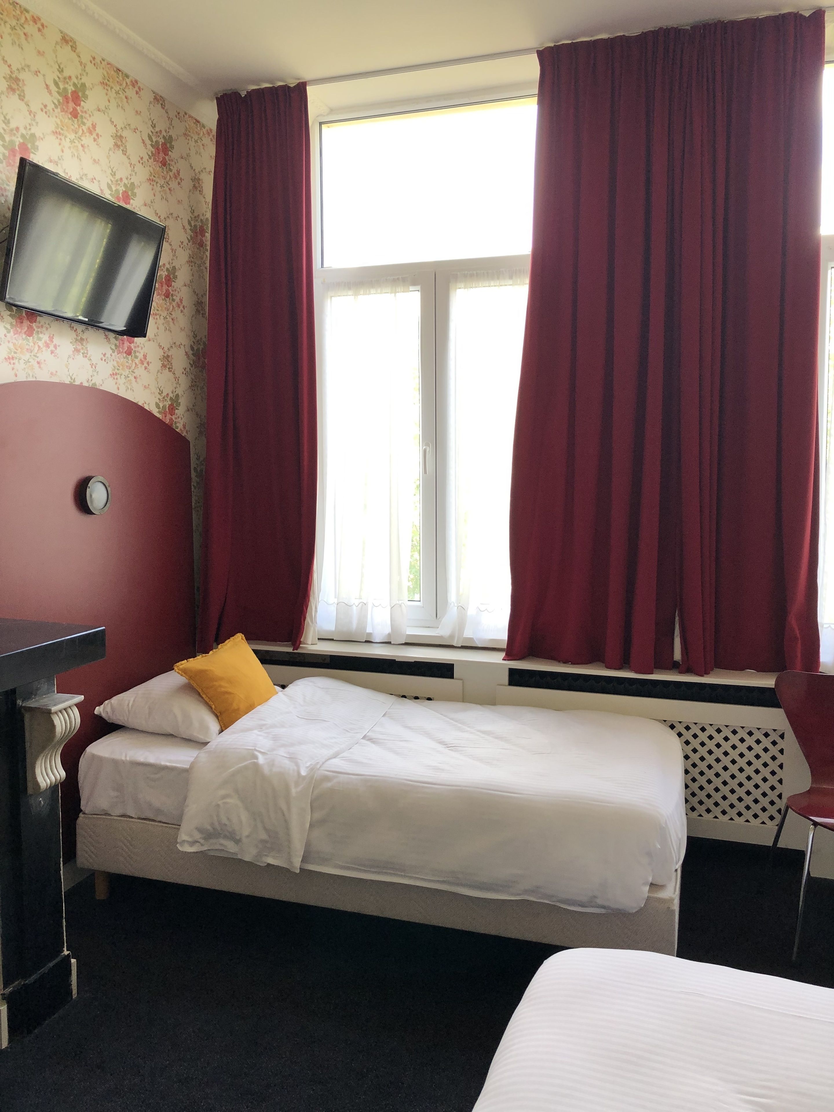 Een hotelkamer met een bed, een bureau, een televisie en een raam met gordijnen.