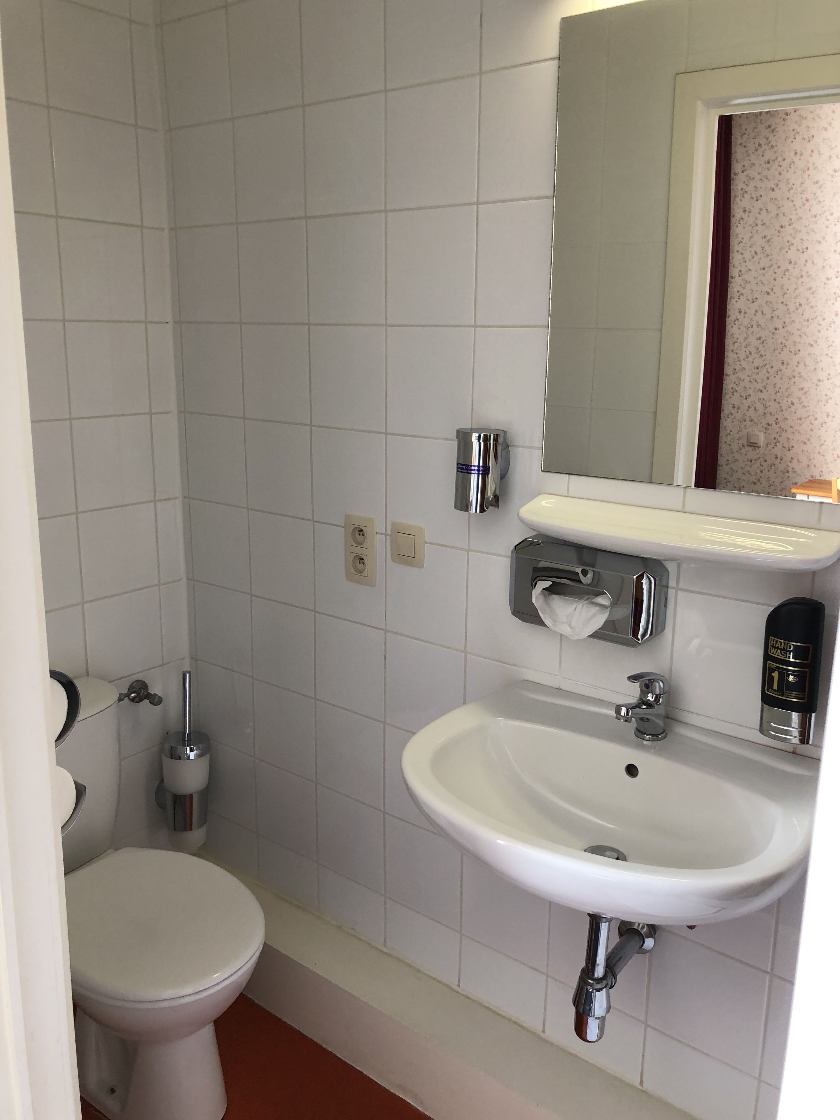 A bathroom with a toilet, sink, mirror, and hand soap dispenser.