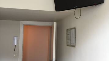A room with a flat-screen TV mounted on the wall, a door leading to another room, a small trash bin, and a wooden table.
