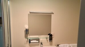 Un baño con lavamanos blanco, un espejo, toallero y cabina de ducha con paredes de vidrio.