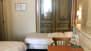 A hotel room with two beds, a wooden table, a chair, a TV mounted on the wall, and a door with a mirror.
