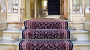 Una imponente escalera con alfombra decorativa y peldaños de mármol que conduce a un rellano en el segundo piso.