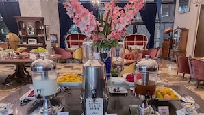 Disposição de buffet com diversos alimentos e bebidas, incluindo um espaço para café com vários dispensadores e uma seleção de frutas.