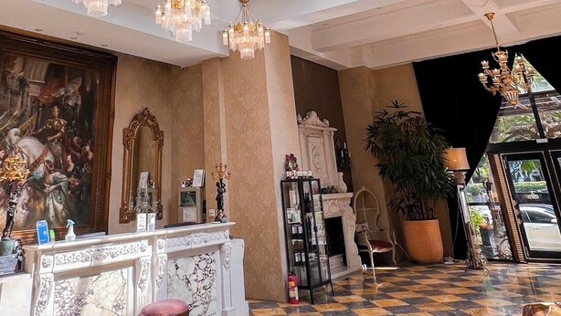 Um hall amplo com teto alto, piso xadrez e uma grande janela que permite entrada de luz natural.