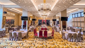 Uma sala de banquetes com mesas redondas, cadeiras vermelhas e um tapete estampado.