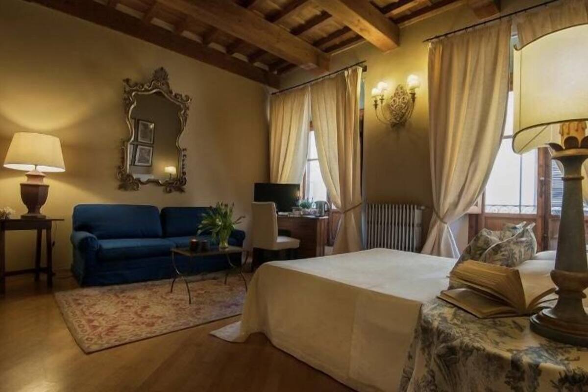 Um quarto aconchegante com uma cama, um sofá azul, uma mesinha e uma luminária.