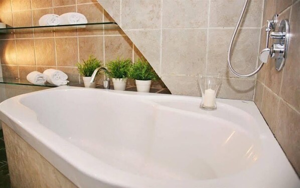A bathroom with a large bathtub, a glass shelf with towels, potted plants, and a glass candle holder. - Capri Moon Guest House (Florence)
