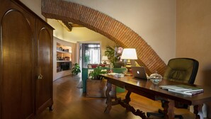 Une pièce spacieuse avec un bureau en bois, un ordinateur portable et une lampe. On aperçoit une chaise et une bibliothèque à l’arrière-plan.