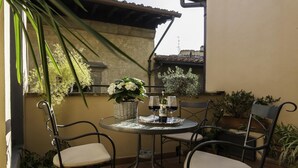 Une petite terrasse extérieure avec une table ronde, deux chaises, un panier de fleurs et deux verres à vin.