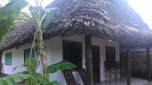 A thatched-roof house with a tiled patio, surrounded by lush greenery. - Cooke Villa (Mtwapa)