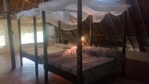 A four-poster bed with a canopy, a wooden floor, and a sloped ceiling. - Cooke Villa (Mtwapa)