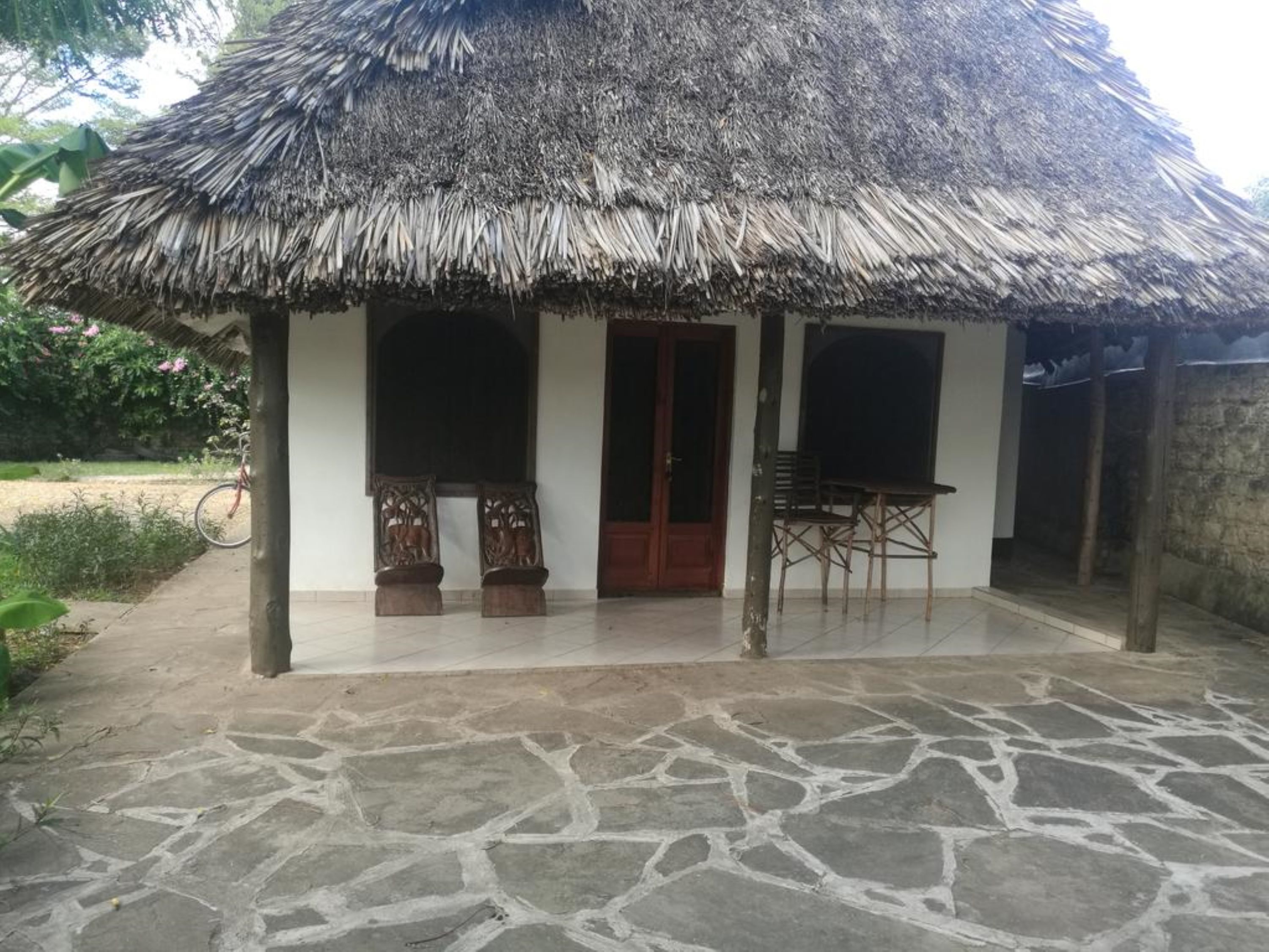 A thatched-roof structure with a tiled floor, wooden benches, and a door.
